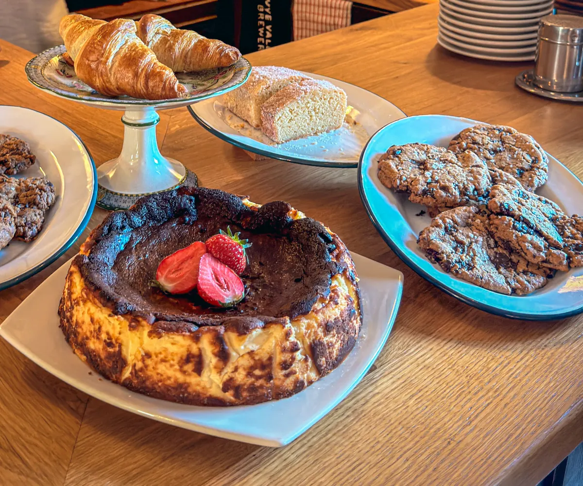 Croissants, a Basque cheesecake with strawberries, cookies and a loaf cake on the café counter.