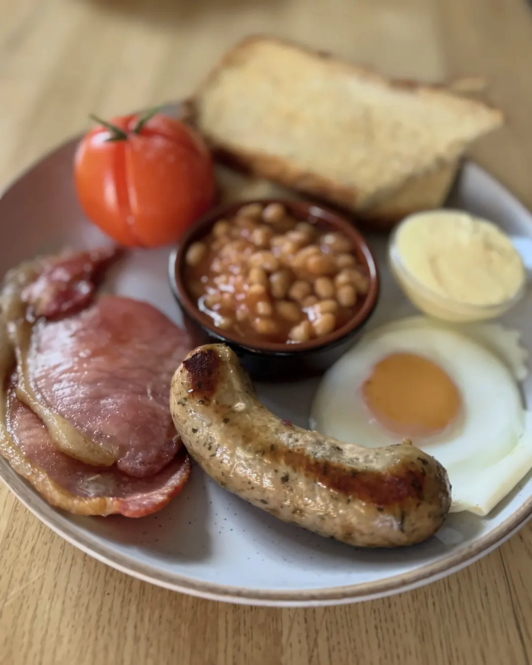 A full English breakfast with bacon, a pork sausage, fried egg, baked beans, a roasted tomato and toast.
