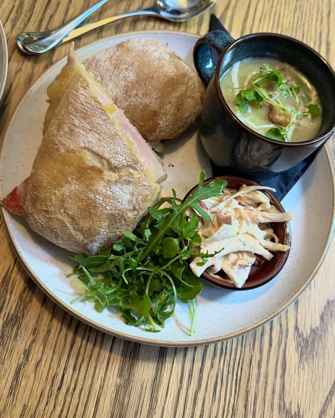 A honey roast ham and cheese sandwich with rocket, slaw and a mug of soup.