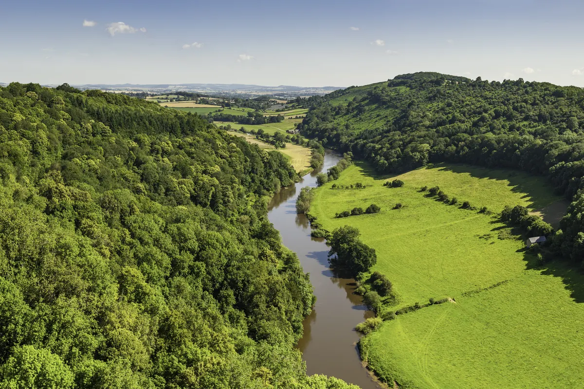 The River Wye winding between steep wooded hills and green fields, seen from high above.
